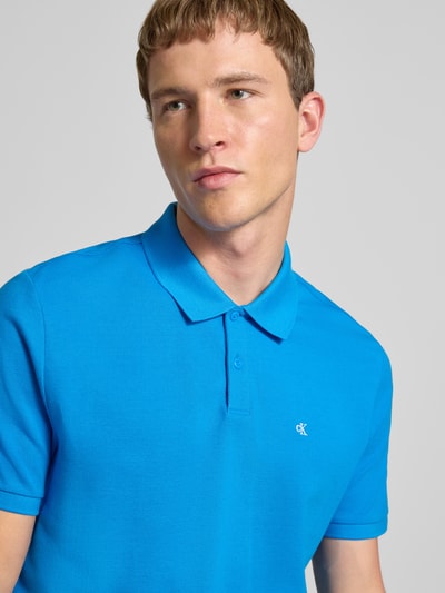Männermodel trägt Straight Fit Poloshirt mit Label-Stitching von Calvin Klein Jeans in kräftigem Blau aus reiner Baumwolle, Nahaufnahme Oberkörper.