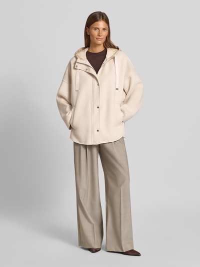 Frauenmodel trägt Jacke mit Kapuze von COMMA in Beige, lockere Passform, glatte Textur, seitliche Eingrifftaschen, Ganzkörperansicht von vorne.