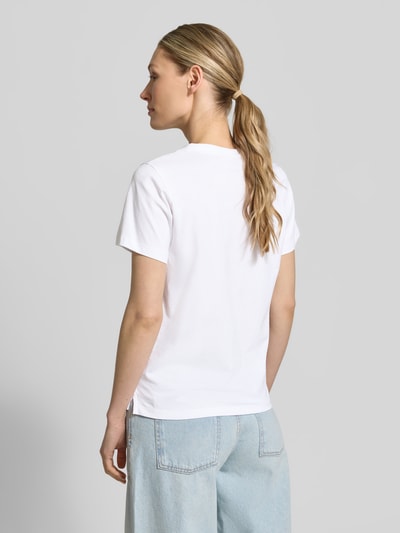 Frauenmodel trägt T-Shirt mit Label-Print und Strasssteinbesatz von Guess aus reiner Baumwolle, Straight Fit, Rückenlänge bei Größe S 59 cm, Ganzkörperansicht Rückansicht.