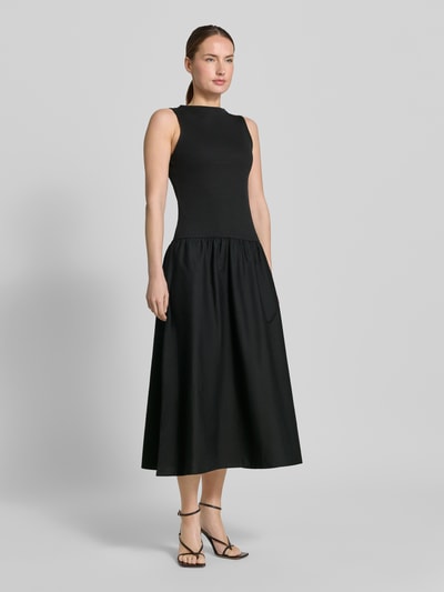 Frauenmodel trägt schwarzes Damen Midikleid mit U-Boot-Ausschnitt Modell 'VALVIN' von Mango, Baumwoll-Mix mit Stretch-Anteil, Taillierter Schnitt, breite Träger, Ganzkörperansicht von vorne.