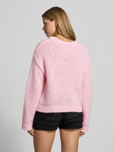 Frauenmodel trägt Relaxed Fit Pullover im Chunky Knit Look Modell 'DORTHEA' von PIECES in Hellrosa, grobe Strickstruktur, Ganzkörperansicht Rückansicht. Damen Pullover von PIECES.