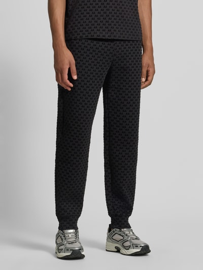 Männermodel trägt Sweatpants im Allover-Look mit Logo-Muster Modell 'PANTALONI' von Armani Exchange, Regular Fit, Nahaufnahme Unterkörper. Baumwoll-Mix mit Stretch-Anteil, elastischer Bund mit Tunnelzug, dunkle Farben, dezentes Muster, Kontext: Herren Sweatpants von Armani Exchange, Innenbeinlänge bei Größe M 77 cm.