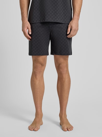 Męski model nosi Shorts aus Baumwolle mit Logo-Muster von JOOP! Collection, czarny, wzór z logo, krój regular fit, bawełna, elastyczny pas, szerokość w rozmiarze M: 42 cm, długość wewnętrzna nogawki: 18 cm, zdjęcie: całkowity widok z przodu