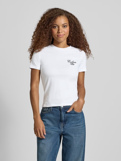 Frauenmodel trägt Slim Fit T-Shirt aus reiner Baumwolle Modell 'Gracious' von Carhartt Work In Progress in Weiß mit Label-Print, Ganzkörperansicht von vorne.