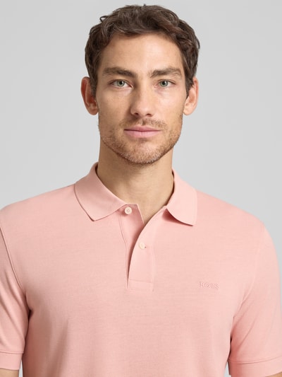 Männermodel trägt Regular Fit Poloshirt aus reiner Baumwolle Modell 'PALLAS' von BOSS in Optik: Unifarben mit Label-Stitching-Applikation, Piqué-Textur, Polokragen, 2-Knopf-Verschluss, Ärmelform: Kurzarm, Nahaufnahme Oberkörper.