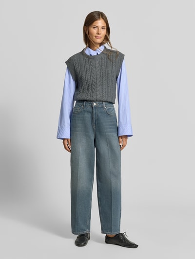 Frauenmodel trägt Hemdbluse aus reiner Baumwolle mit integrierter Krawatte von MYON, taillierte Passform, helle Blautöne, Hemdblusenkragen, lange Ärmel, darunter graues Stricktop, kombiniert mit weiter Jeans, weiche Stofftextur, Ganzkörperansicht von vorne.