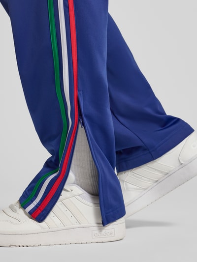 Männermodel trägt Regular Fit Sweatpants mit mehrfarbigen Kontraststreifen Modell 'FIREBIRD TP' von adidas Originals, Detailaufnahme Unterschenkel, blaue Farbe, seitliche Reißverschlusstaschen, elastischer Bund, Logo-Stitching.
