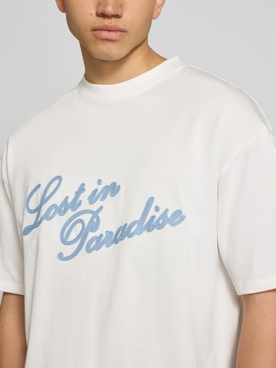 Männermodel trägt T-Shirt mit Logo- und Statement-Stitching von REVIEW, weiße Baumwolle, gerader Schnitt, Nahaufnahme Oberkörper.
