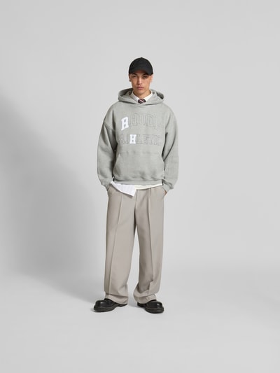 Männermodel trägt Oversized Hoodie mit Logo-Print von RHUDE aus Baumwoll-Mix, Oversized-Fit, Känguru-Tasche, elastische Abschlüsse, Ganzkörperansicht von vorne