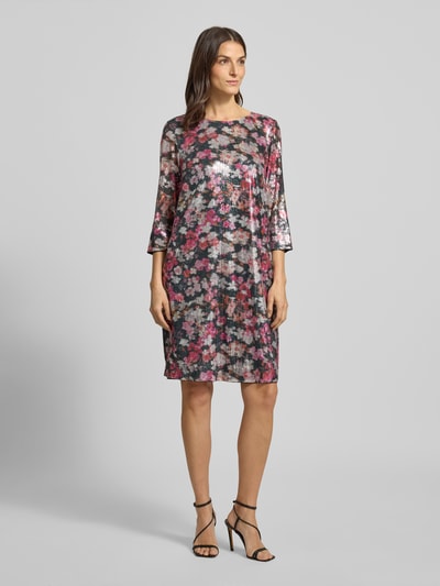 Kobiece modelka nosi Knielanges Kleid mit Allover-Muster und Paillettenbesatz von Christian Berg Woman, kolorowy kwiatowy wzór, okrągły dekolt, rękaw o dł. 3/4, prosty krój, czarna i różowa kolorystyka, długość do kolan, długość tyłu w rozmiarze 36: 96 cm, szerokość w rozmiarze 36: 48 cm, długość rękawa 47 cm, widok całej sylwetki z przodu.