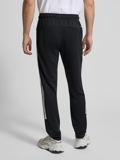 Männermodel trägt Sweatpants mit Label-Print von adidas Training, schwarzer Stoff, Lockerer-Schnitt, Reißverschlusstaschen, Ganzkörperansicht Rückansicht. Innenbeinlänge bei Größe M: 76 cm. Elastischer Bund.