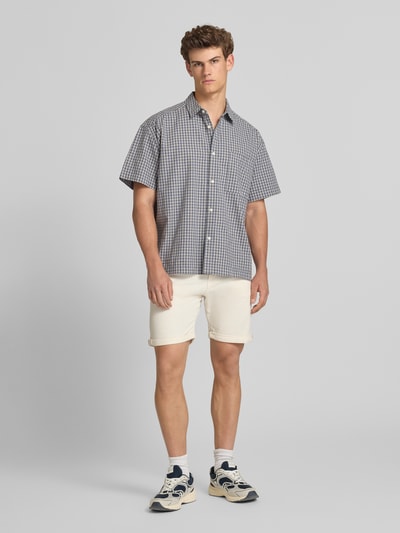 Männermodel trägt Jeansshorts mit Umschlag und Eingrifftaschen Modell 'RICK ALLEN' von Jack & Jones aus Baumwoll-Elasthan-Mix, Regular-Fit, Farbton hell, Struktur glatt, Bundweite 43 cm, Innenbeinlänge 20 cm, Ganzkörperansicht von vorne.