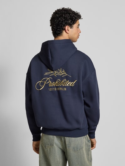 Männermodel trägt Oversized Hoodie mit Label-Stitching von PROHIBITED aus dunkelblauem Baumwoll-Mix, Rückenlänge 67 cm, Känguru-Tasche, Gerippte Abschlüsse, Rückansicht Ganzkörperansicht.