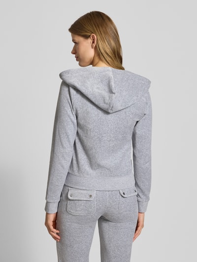 Frauenmodel trägt Sweatjacke mit Label-Stitching Modell 'ROBERTSON' von Juicy Couture in Grau, Material-Mix mit Stretch-Anteil, Regular-Fit, Kapuze mit Tunnelzug, Reißverschluss, Känguru-Tasche, Ganzkörperansicht Rückansicht.