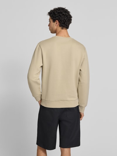 Männermodel trägt Sweatshirt mit Rundhalsausschnitt und Label-Stitching von Carhartt Work In Progress im Regular-Fit aus Baumwoll-Elasthan-Mix in Beige, schwarze Shorts, glatte Oberfläche, Rückenlänge bei Größe M: 68 cm, Ärmellänge bei Größe M: 65 cm, Ganzkörperansicht Rückansicht.