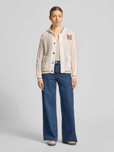 Frauenmodel trägt Regular Fit Strickjacke mit Kapuze von monari, Reine Baumwolle, Lochmuster, Logo-Detail, AufgesetzteTaschen, Zierbesatz, durchgängige Knopfleiste, elastische Abschlüsse, Rückenlänge 56 cm, Ärmellänge 59 cm, Ganzkörperansicht von vorne.