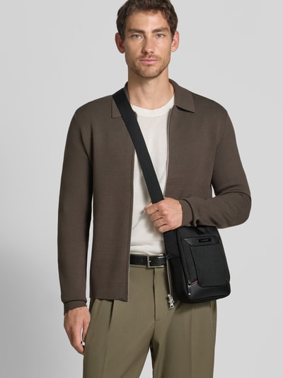 Männermodel trägt Crossbody Bag mit Logo-Detail Modell 'Pro DLX' von Samsonite in Schwarz, Struktur-Textur, Ganzkörperansicht von vorne. Kontext: Herren Crossbody Bag, geteiltes Hauptfach mit Reißverschluss, verstellbarer Trageriemen, Breite 19 cm, Länge 27 cm, Tiefe 8 cm, Schulterriemen 90 cm.