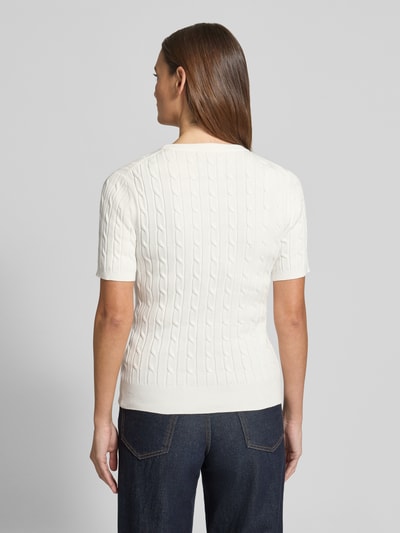 Modelka nosi Strickshirt mit Zopfmuster und Label-Stitching od Gant, mieszanka bawełny, krój slim fit, okrągły dekolt, ścieg warkoczowy, wyhaftowane logo, długość tyłu w rozmiarze S: 57 cm, długość rękawów w rozmiarze S: 24 cm, kolor jasny, faktura dzianiny, widok całej sylwetki z tyłu.