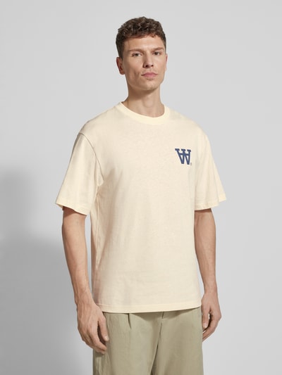 Męski model nosi Relaxed Fit T-Shirt mit Logo-Print Modell 'Liam' od Wood Wood, bawełna, jasny beż, nadruk, widok z przodu, zdjęcie całej sylwetki.