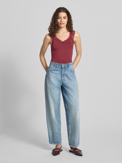Frauenmodel trägt Slim Fit Tanktop aus Viskose-Mix Modell 'BARBERA' von PIECES in Dunkelrot mit Spitzenbesatz, kombiniert zu blauen Jeans, Ganzkörperansicht von vorne.
