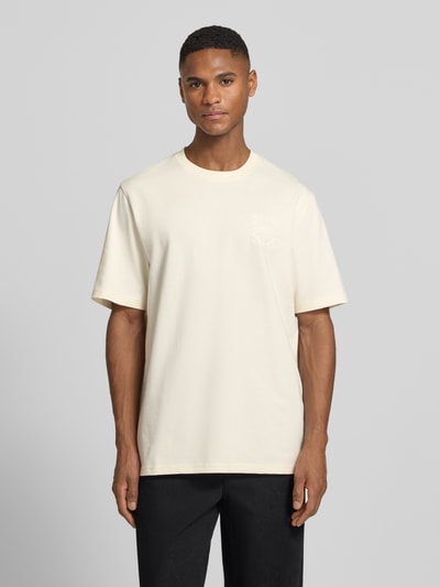 Männermodel trägt T-Shirt mit Label-Print Modell 'Ben Goods' von Les Deux aus Bio-Baumwolle in Creme, gerader Schnitt, Ganzkörperansicht von vorne.