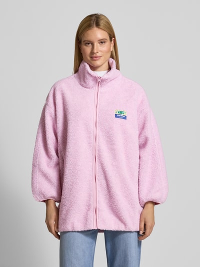 Vrouwenmodel draagt oversized jas met opstaande kraag model 'HOKTOWN' van American Vintage, teddy fleece, lichtroze, rits, labeldetail, steekzakken, volledige voorkant, volledige lichaamsweergave van voren.