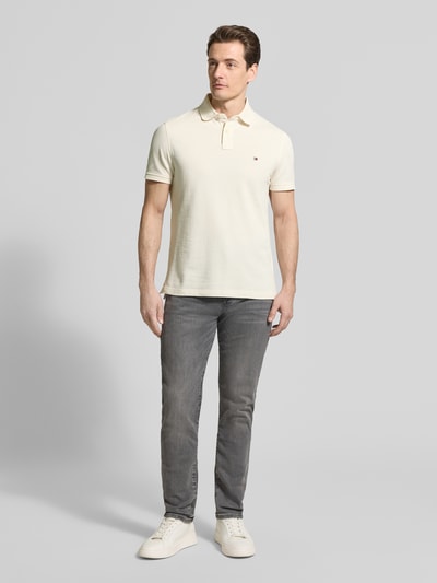 Mannelijk model draagt Regular Fit Poloshirt uit katoenmix van Tommy Hilfiger, look: effen, pasvorm: regular fit, gestikt logo, polokraag, 2-knoopsluiting, korte mouw, rompzoom met split, materiaalverwerking: piqué, kleur: licht, materiaal: katoenmix. Volledige lichaamsopname van voren.