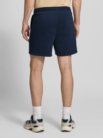 Męski model nosi Regular Fit Shorts aus Baumwoll-Mix von Tommy Jeans, efekt: jednolity kolor, detal z logo, tunel, kieszeń z tyłu, krój regular fit, mieszanka bawełny, dzianina dresowa, widok całej sylwetki z tyłu.