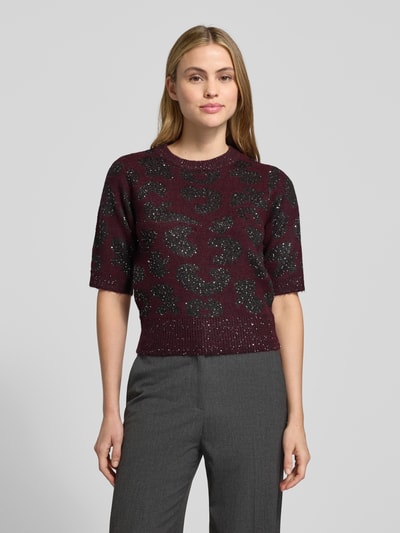 Vrouwenmodel draagt Shaped Fit Strickpullover met wol-aandeel model 'ZUZU 2/4 O-NECK PULLOVER' van Vero Moda, uni bordeaux, abstract patroon, ronde hals, korte mouw, glanzende pailletten, gebreide textuur, voorkant totaalbeeld.