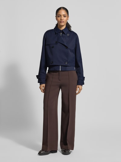 Vrouwenmodel draagt Trenchcoat mit Ärmelriegeln van monari in regular fit, marineblauw, knoopsluiting, opstaande kraag, tweerijig, detailopname volledige voorkant.