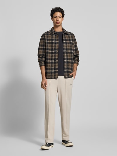 Męski model nosi Spodnie dresowe z wyhaftowanym logo Model 'Motus Track Pants' od Pegador, mieszanka bawełny, krój regular fit, kieszeń z tyłu, długość wewnętrzna nogawki 73 cm w rozmiarze M, kolor beżowy, gładka tekstura, całkowity widok z przodu.