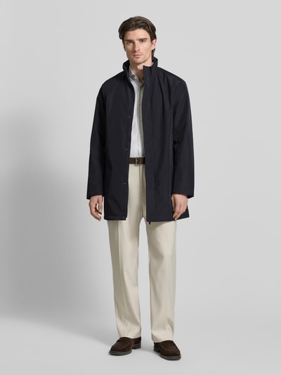 Männermodel trägt Trenchcoat mit Stehkragen von ARMANI EXCHANGE in Dunkelblau, gerader Schnitt, verdeckter Reißverschluss, Ganzkörperansicht von vorne.