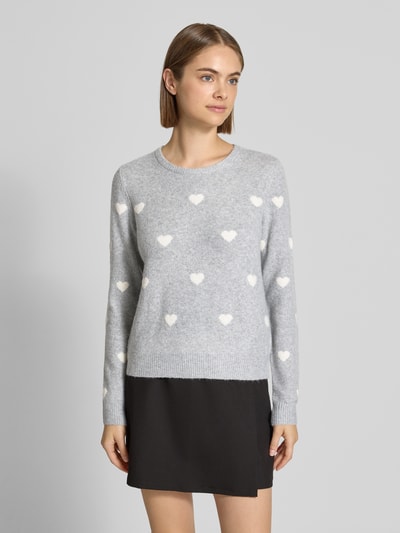 Kobiece modelka nosi sweter z dzianiny 'Strickpullover mit geripptem Saum' od REVIEW, elastyczna mieszanka materiałów, prosty krój, okrągły dekolt, prążkowany dół, długość tyłu w rozmiarze S: 47 cm, długość rękawów: 64 cm, szaro-biały kolor z motywem serc, widoczne kontrasty faktur, widok na całe ciało z przodu.