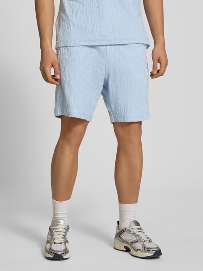 Męski model nosi Regular Fit Shorts aus Frottee od HUGO w jasnoniebieskim kolorze, faktura frottee, przód, krój regular fit, logo, kieszenie po bokach, tylna kieszeń, ściągacz w pasie, zdjęcie całej sylwetki z przodu.