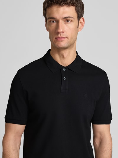 Männermodel trägt Poloshirt aus Baumwolle von MARC O’POLO DENIM in Schwarz, klassische Knopfleiste, Logo, Nahaufnahme Oberkörper.