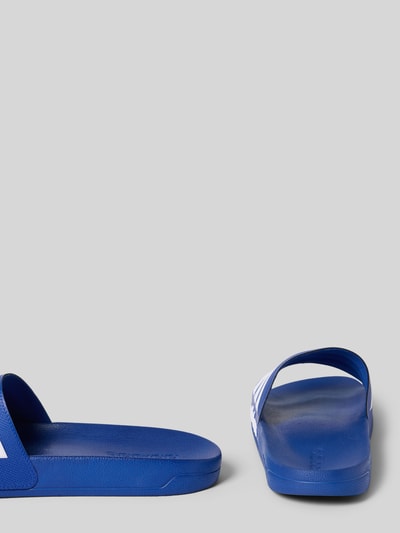 Productfoto, Badeschuhe mit Kontraststreifen van adidas Sportswear in effen blauw met witte details, afgeronde neus, platte zool, gestructureerde zool, productaanzicht vanuit de zijkant en achterkant.
