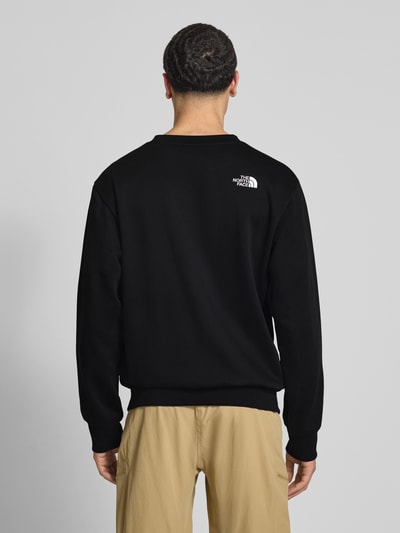 Męski model nosi Relaxed Fit Sweatshirt mit Label-Stitching Modell 'ESSENTIAL' od The North Face, bawełniany miks, czarny, elastyczne wykończenia, widok całej sylwetki z tyłu.