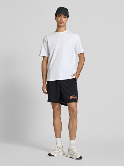 Männermodel trägt Regular Fit Shorts mit Logo-Print von KARL KANI in Schwarz mit Strukturmuster, elastischem Bund, Ganzkörperansicht von vorne.
