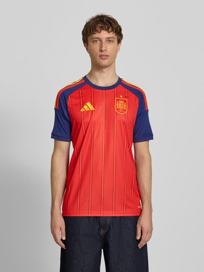 Männermodel trägt Spanien Heimtrikot 2026 von adidas, Herren T-Shirt mit Optik:Allover-Muster, Slim-Fit, Logo-Patch, Logo-Detail, Rundhals, Kurzarm, Ganzkörperansicht von vorne.