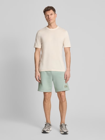 Männermodel trägt Sweatshorts mit Logo und elastischem Bund von GAP in Mintgrün, Baumwoll-Mix, Regular-Fit, Eingrifftaschen, Ganzkörperansicht von vorne.