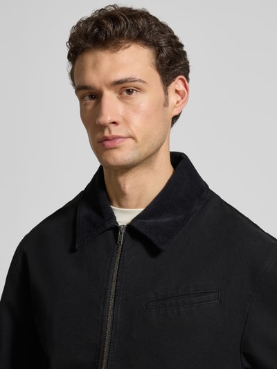 Männermodel trägt Jacke mit Zweiwege-Reißverschluss Modell 'Bo' von Wood Wood aus schwarzer Baumwolle, Nahaufnahme Oberkörper. Regular Fit, Umlegekragen, sichtbarer Reißverschluss und Brusttasche.