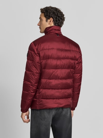 Männermodel trägt Regular Fit Steppjacke mit Stehkragen von JOOP! COLLECTION in Dunkelrot, glänzende Oberfläche, Ganzkörperansicht Rückansicht.