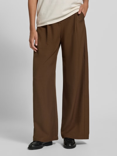 Männermodel trägt spodnie z szerokimi nogawkami z zakładkami w pasie Wide Leg Hose mit Bundfalten Modell 'JOKER' von SUNCOO PARIS, Mieszanka materiałów z dodatkiem wiskozy, kolor brązowy, Szerokość w rozmiarze S: 35 cm, Długość wewnętrzna nogawki w rozmiarze S: 79 cm, widok całej sylwetki z przodu.