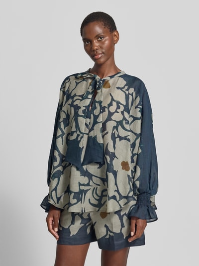 Modelka nosi bluzkę 'Bluse mit Schluppe und Volantärmeln' od Luisa Cerano, mieszanka lyocellu z dodatkiem ramii, krój loose fit, wycięcie w kształcie łezki z kokardą, rękawy z falbanami i marszczonym detalem, długość tyłu w rozmiarze 36: 74 cm, długość rękawów: 65 cm, wielokolorowy wzór, tekstura lekko przezroczysta, widok całej sylwetki z przodu.