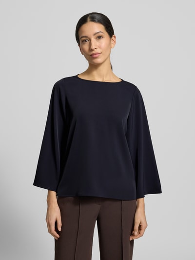 Modelka nosi Blusenshirt mit Rundhalsausschnitt von comma, czarny materiał z domieszką stretchu, luźny krój, widok całej sylwetki z przodu. Długość tyłu w rozmiarze 36: 59 cm, długość rękawa w rozmiarze 36: 52 cm.