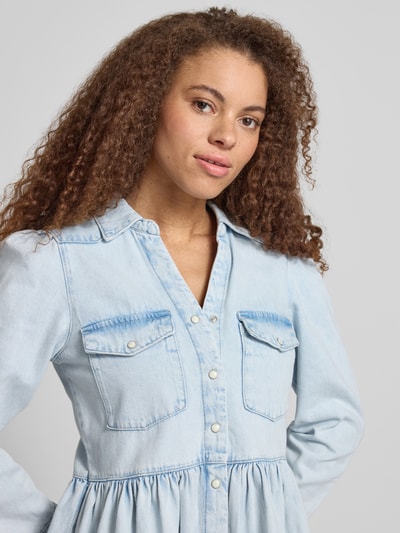 Frauenmodel trägt Mini-Jeanskleid aus reiner Baumwolle Modell 'CYRUS' von Only in heller Denim-Optik mit V-Ausschnitt, Nahaufnahme Oberkörper.