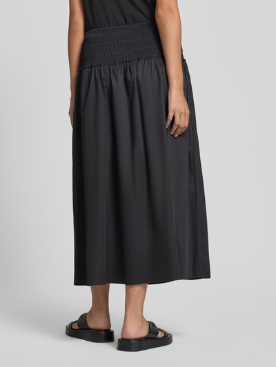 Frauenmodel trägt Midirock mit Smok-Detail von Comma aus elastischem Baumwoll-Mix in Schwarz, A-Linie, Ganzkörperansicht Rückansicht.
