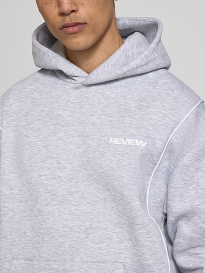 Männermodel trägt Hoodie mit Logo und Känguru-Tasche von REVIEW, Baumwoll-Mix, Regular-Fit, meliert, Nahaufnahme Oberkörper.