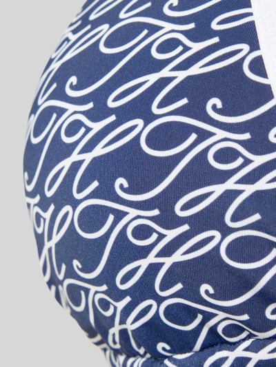 Frauenmodel trägt Neckholder Bikini-Oberteil mit Label-Print von TOMMY HILFIGER in Blau mit weißem Allover-Muster, Detailaufnahme.