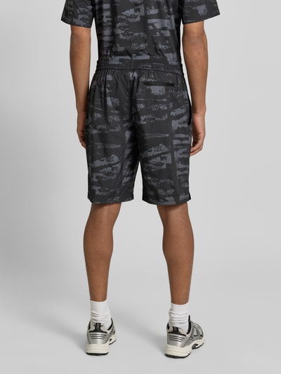 Männermodel trägt Regular Fit Shorts mit Allover-Muster Modell 'Globe AOP' von BOSS Green in dunklem Camouflage, Ganzkörperansicht Rückansicht.